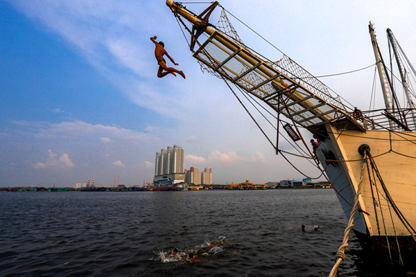 Sejumlah anak-anak asyik berenang di antara kapal-kapal yang bersandar di Pelabuhan Kaliadem, Muara Angke, Jakarta utara, Minggu (23/5/2021).