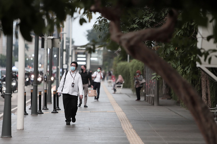 Pekerja kantor mengenakan masker berjalan di pedestrian Jalan MH Thamrin, Jakarta Pusat, Senin (24/5/2021).