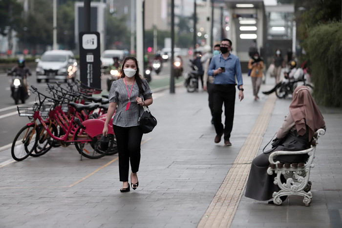 Pekerja kantor mengenakan masker berjalan di pedestrian Jalan MH Thamrin, Jakarta Pusat, Senin (24/5/2021).