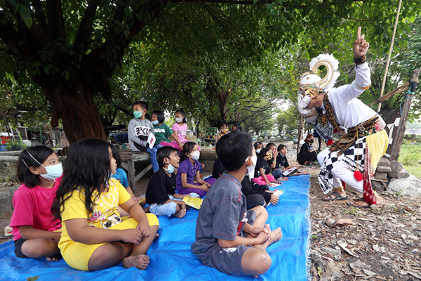 Pendongeng Harris Rizki Akhiruddin mengenakan kostum Kera Putih Hanoman menghibur anak-anak di komplek pemakaman Rangkah Surabaya, Jawa Timur, Rabu (26/5/2021).