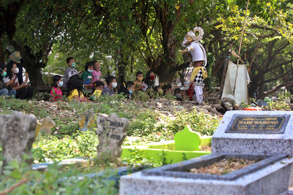 Pendongeng Harris Rizki Akhiruddin mengenakan kostum Kera Putih Hanoman menghibur anak-anak di komplek pemakaman Rangkah Surabaya, Jawa Timur, Rabu (26/5/2021).