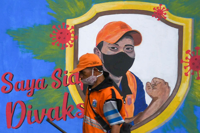 Petugas dan warga saat melintas di depan mural himbauan pandemi Covid-19 di Jakarta Selatan, Selasa (15/6/2021).