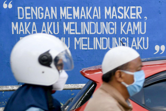 Petugas dan warga saat melintas di depan mural himbauan pandemi Covid-19 di Jakarta Selatan, Selasa (15/6/2021).