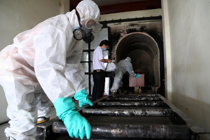 Petugas Krematorium mengenakan Hazmat dan APD memasukkan peti jenazah kedalam tungku pembakaran di Krematorium Keputih, Surabaya, Selasa (29/6/2021).