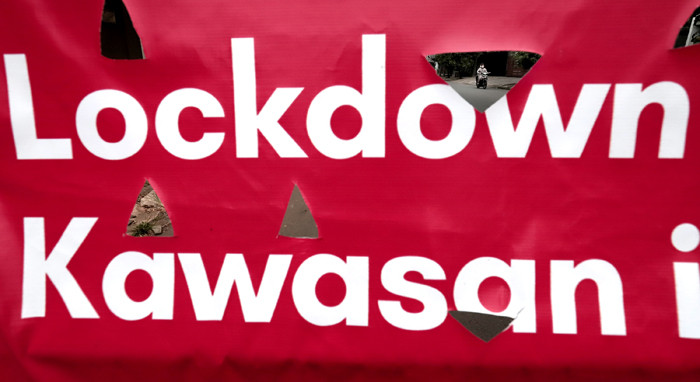Pengendara melintasi spanduk bertuliskan Lockdown Mikro RW 08 Kawasan Ini Tertutup di kawasan Puri Gading, Kota Bekasi, Jawa Barat, Senin (5/7/2021).