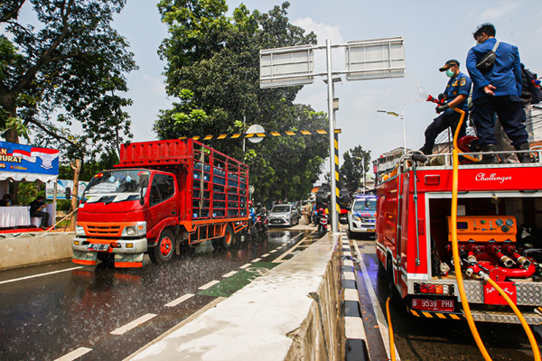 Petugas Pemadam Kebakaran meyemprotkan cairan disinfektan ke pengendara di Jalan Raya Lenteng Agung, Jakarta Selatan, Senin (5/7/2021).