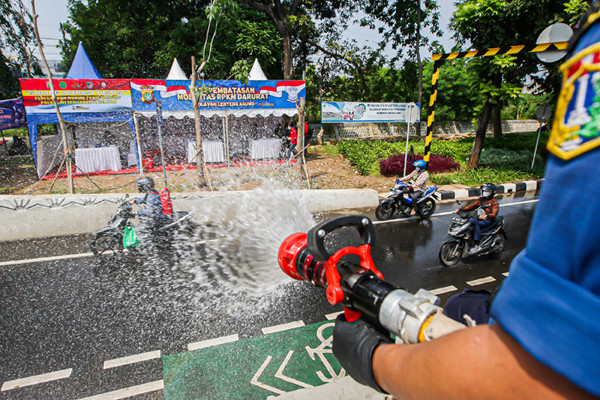 Petugas Pemadam Kebakaran meyemprotkan cairan disinfektan ke pengendara di Jalan Raya Lenteng Agung, Jakarta Selatan, Senin (5/7/2021).