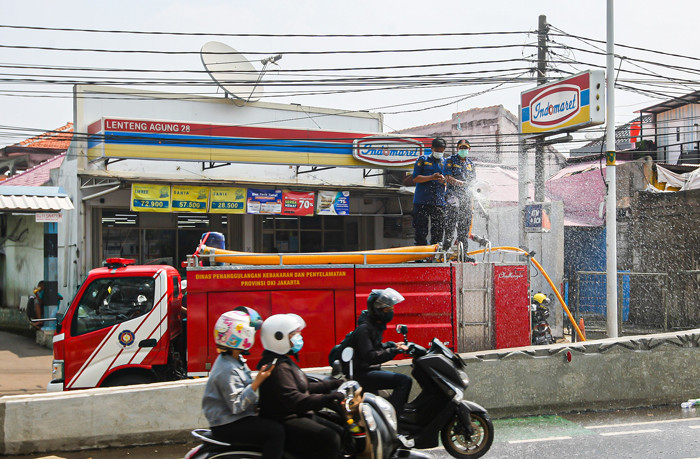 Petugas Pemadam Kebakaran meyemprotkan cairan disinfektan ke pengendara di Jalan Raya Lenteng Agung, Jakarta Selatan, Senin (5/7/2021).