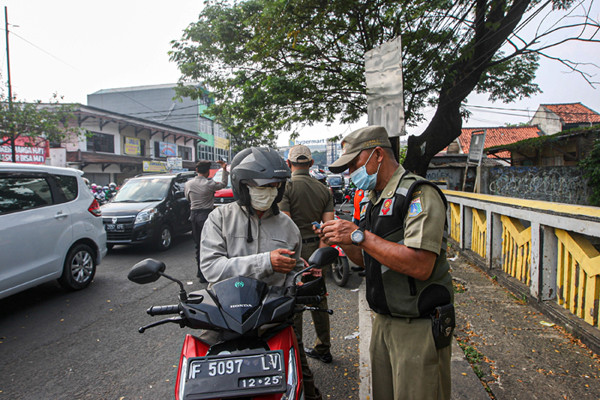 Petugas memeriksa KTP warga yang ingin melewati penyekatan di Jalan Molek, Pondok Gede, Kota Bekasi, Jawa Barat, Minggu (11/7/2021).