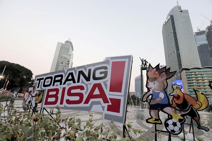 Pengendara melintas di dekat maskot dan slogan Pekan Olahraga Nasional (PON) XX Papua di Bundaran Hotel Indonesia, Jakarta, Jumat (16/7/2021).