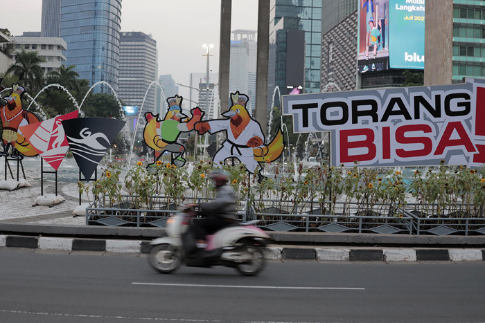 Pengendara melintas di dekat maskot dan slogan Pekan Olahraga Nasional (PON) XX Papua di Bundaran Hotel Indonesia, Jakarta, Jumat (16/7/2021).