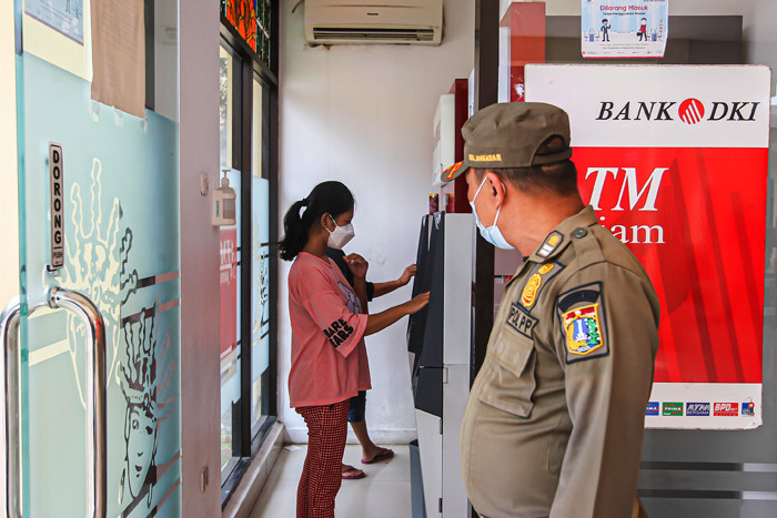 Petugas Satpol PP mengatur antrean warga yang ingin mencairkan Bantuan Langsung Tunai di Kecamatan Makasar, Jakarta Timur, Selasa (20/7/2021).