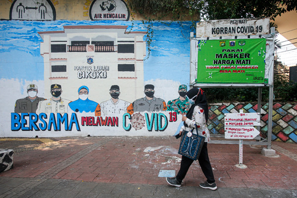 Pejalan kaki melintas di dekat tembok dengan mural melawan Covid-19 di kawasan Cikokol, Cawang, Jakarta, Rabu (28/7/2021).