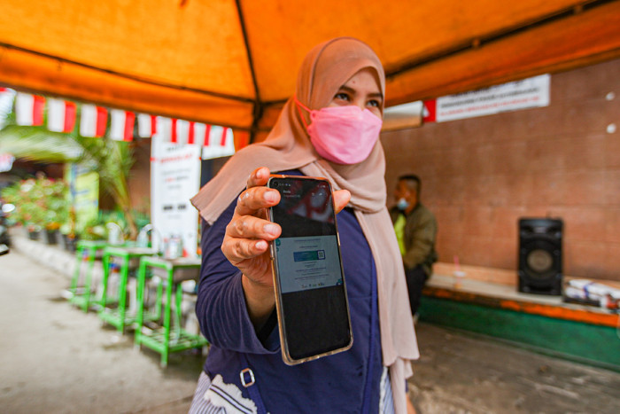Pengunjung menunjukan sertifikat bukti telah melakukan vaksin kepada petugas sebelum masuk ke Gedung Pasar Jatinegara, Jakarta Timur, Senin (9/8/2021).