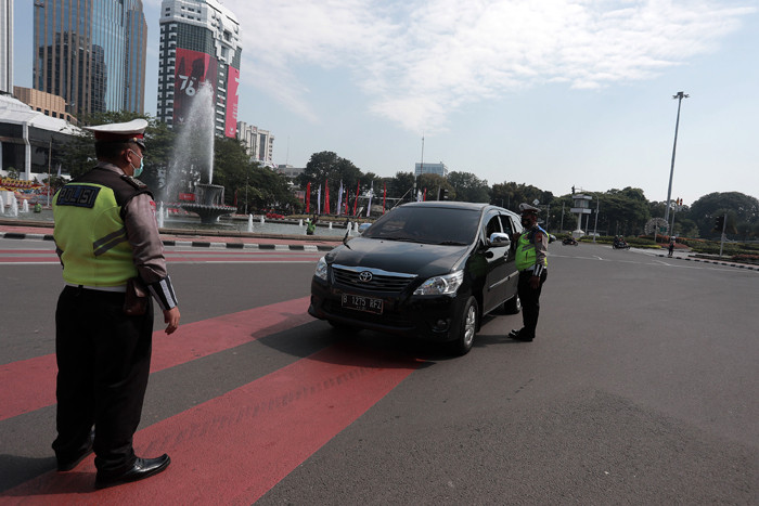 Petugas kepolisian melakukan pengaturan kendaraan saat pelaksanaan pengendalian mobilitas ganjil genap di Jalan MH Thamrin, Jakarta, Kamis (12/8/2021).