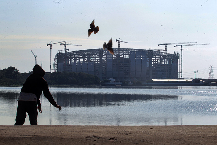 Warga melatih burung merpati dengan latar belakang proyek pembangunan Jakarta International Stadium di Tanjung Priok, Jakarta Utara, Kamis (12/8/2021).