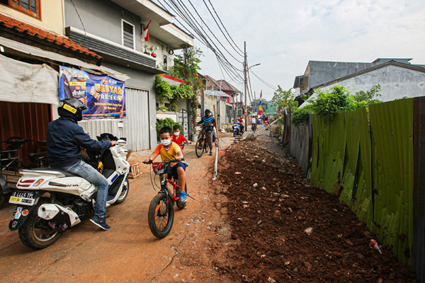 Warga melintas di Jalan Gudang Air yang mengalami keretakan di Kelurahan Rambutan, Kecamatan Ciracas, Jakarta Timur, Minggu (22/8/2021).
