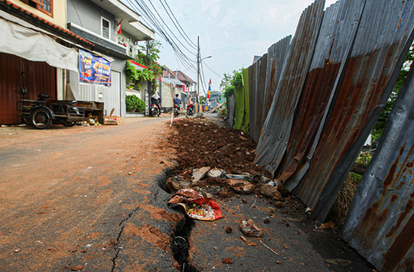 Warga melintas di Jalan Gudang Air yang mengalami keretakan di Kelurahan Rambutan, Kecamatan Ciracas, Jakarta Timur, Minggu (22/8/2021).