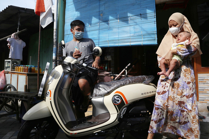 Sekti Bagus Saputro bersama istri dan bayinya berpose dengan satu unit sepeda motor Scoopy di Desa Kepuh Waru, Sidoarjo, Jawa Timur, Senin (23/8/2021).