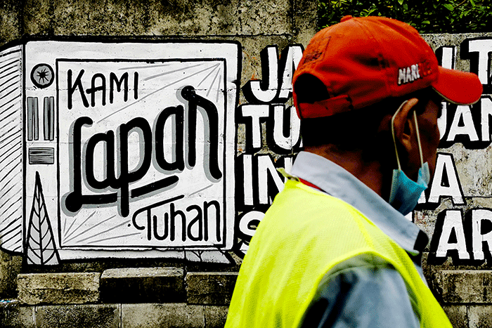 Warga saat melintas dengan berlatar belakang mural yang bertuliskan 'kami lapar tuhan' di Jakarta Pusat, Selasa (24/8/2021).