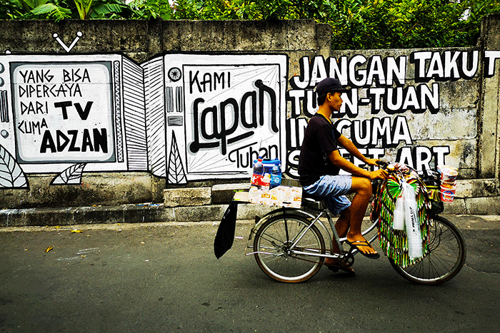 Warga saat melintas dengan berlatar belakang mural yang bertuliskan 'kami lapar tuhan' di Jakarta Pusat, Selasa (24/8/2021).