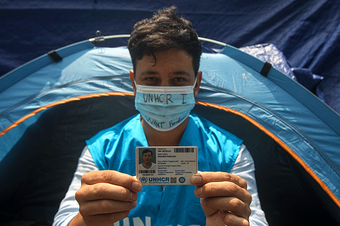 Seorang pencari suaka asal Afghanistan bermain telepon genggam di dalam tenda di trotoar jalan kawasan Kebon Sirih, Jakarta Pusat, Jumat (27/8/2021).