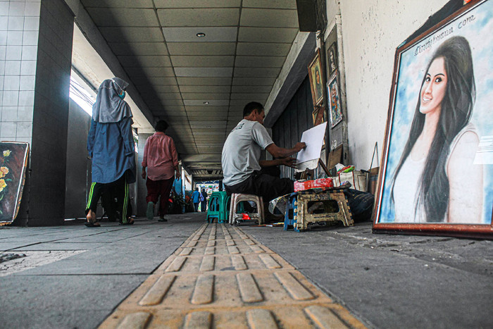Seorang pelukis jalanan sedang menggambar potret wajah pelanggan di lorong kawasan Kota Tua, Jakarta Barat, Rabu (15/9/2021).