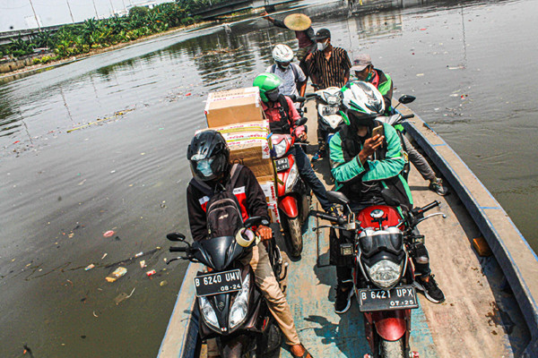 Sejumlah pengendara motor menggunakan jasa perahu eretan di kawasan Kali Angke, Kapuk, Jakarta Barat, Senin (20/9/2021).