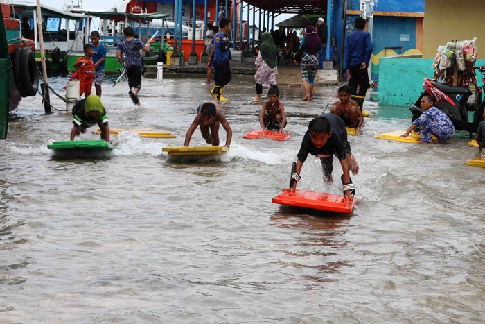 Anak-anak bermain luapan air laut yang menggenangi dermaga di pulau Panggang Kepulauan Seribu Utara, Provinsi DKI Jakarta, Selasa (7/12/2021).
