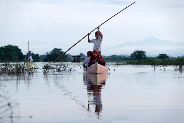 Sejumlah murid menggunakan perahu saat melintasi area persawahan yang terendam banjir di Kelurahan Tamangapa, Makassar, Rabu (15/12/2021).