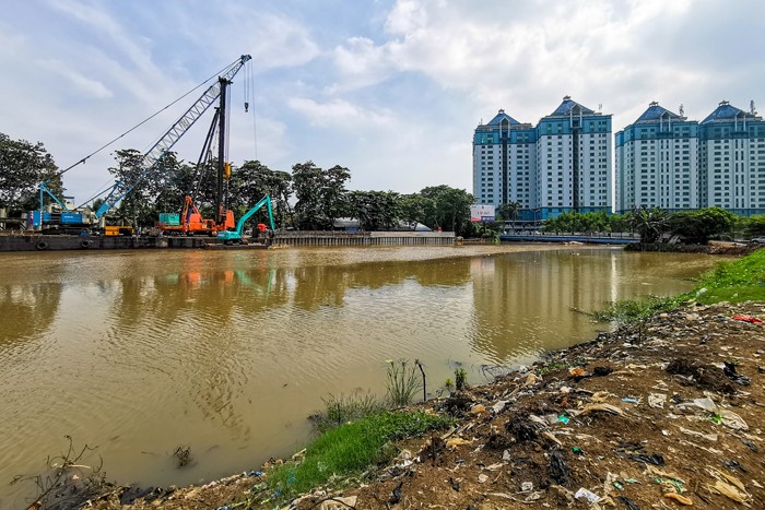 Pekerja dengan alat berat saat menyelesaikan pemasangan dinding turap atau sheetpile di aliran kali PIK, Jakarta Utara, Selasa (21/12/2021).