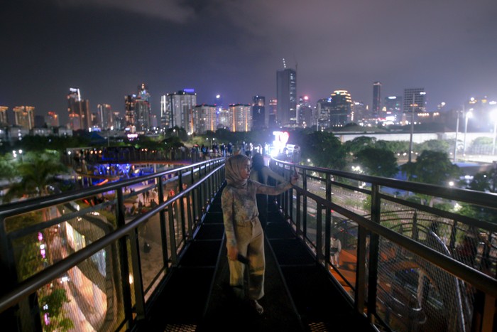 Pengunjung berswafoto dengan latar belakang lansekap perkotaan di Skywalk, Senayan Park, Jakarta, Rabu (29/12/2021).