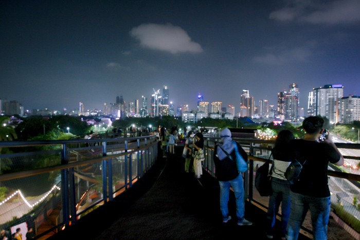 Pengunjung berswafoto dengan latar belakang lansekap perkotaan di Skywalk, Senayan Park, Jakarta, Rabu (29/12/2021).