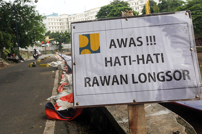 Warga melintas di samping jalan yang amblas di Jalan Inspeksi Kali Ciliwung, Jatinegara, Jakarta Timur.