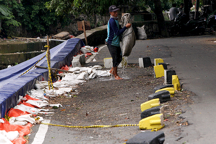 Warga melintas di samping jalan yang amblas di Jalan Inspeksi Kali Ciliwung, Jatinegara, Jakarta Timur.