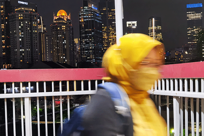 Pekerja melintas berlatar belakang gedung perkantoran di Jembatan Penyeberangan Orang, Jakarta, Senin (9/5/2022).
