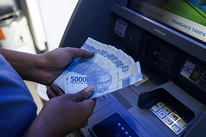 Seorang warga menunjukkan uang sebelum melakukan setor tunai di salah satu Anjungan Tunai Mandiri (ATM) kawasan Jakarta Timur, Kamis, (9/6/2022).