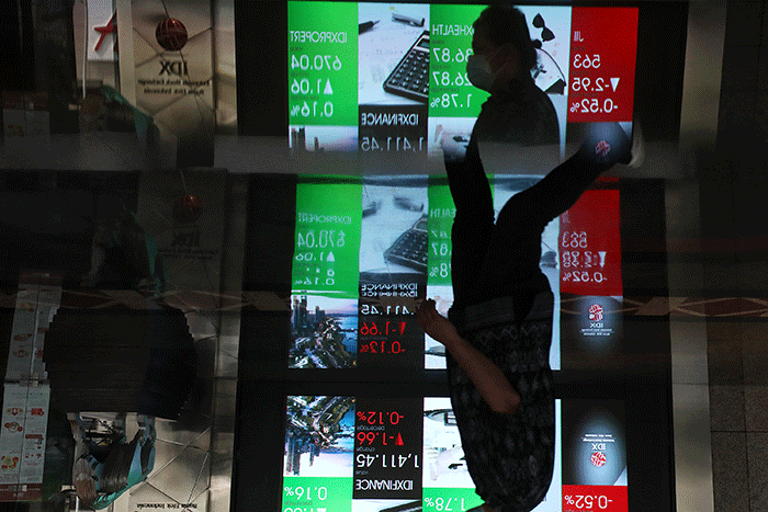 Karyawan melintas di depan layar pergerakan indeks harga saham gabungan (IHSG) di Bursa Efek Indonesia (BEI), Jakarta, Senin (11/7/2022).