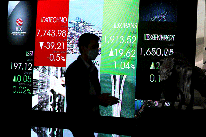 Karyawan melintas di depan layar pergerakan indeks harga saham gabungan (IHSG) di Bursa Efek Indonesia (BEI), Jakarta, Senin (11/7/2022).