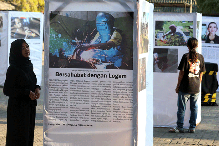 Pengunjung mengamati foto cerita karya Unit Kegiatan Mahasiswa (UKM) Communication Photography Club (CIPHOC).