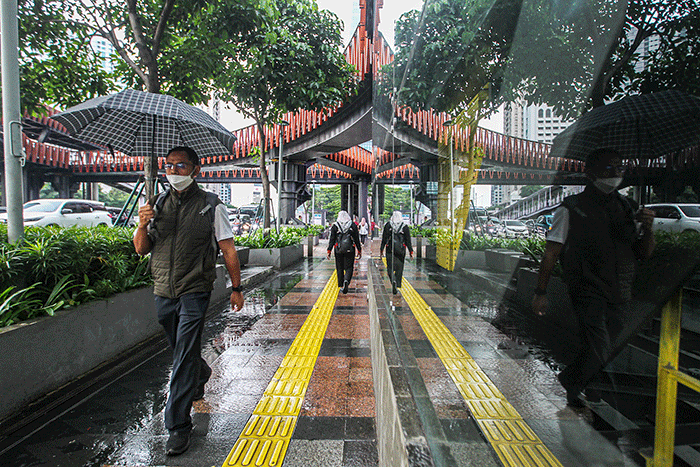 Warga dengan mengunakan payung menerjang hujan saat jam pulang kerja di kawasan Jalan Jenderal Sudirman, Jakarta, Senin (12/12/2022).