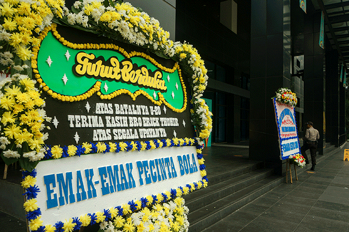 Pekerja melintas dekat karangan bungan di halaman kantor PSSI, Senayan, Jakarta, Kamis (30/3/2023).