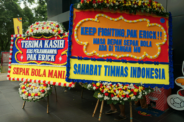 Pekerja melintas dekat karangan bungan di halaman kantor PSSI, Senayan, Jakarta, Kamis (30/3/2023).