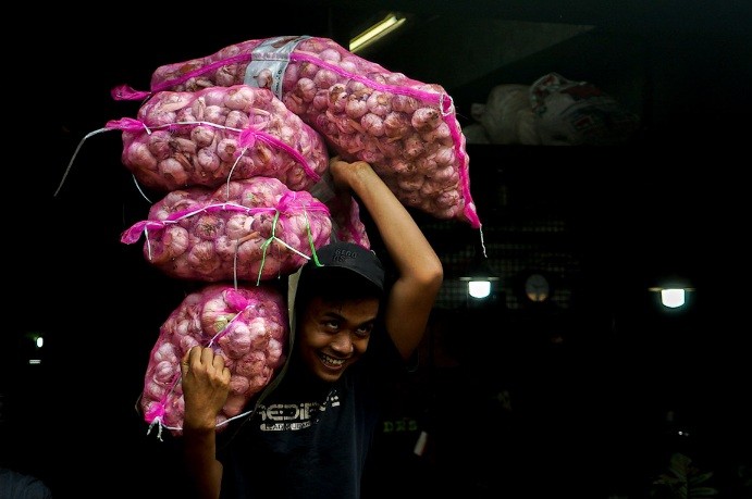Pekerja memindahkan stok bawang putih dari gudang ke atas mobil di Pasar Induk Kramat Jati, Jakarta, Selasa (30/5/2023).